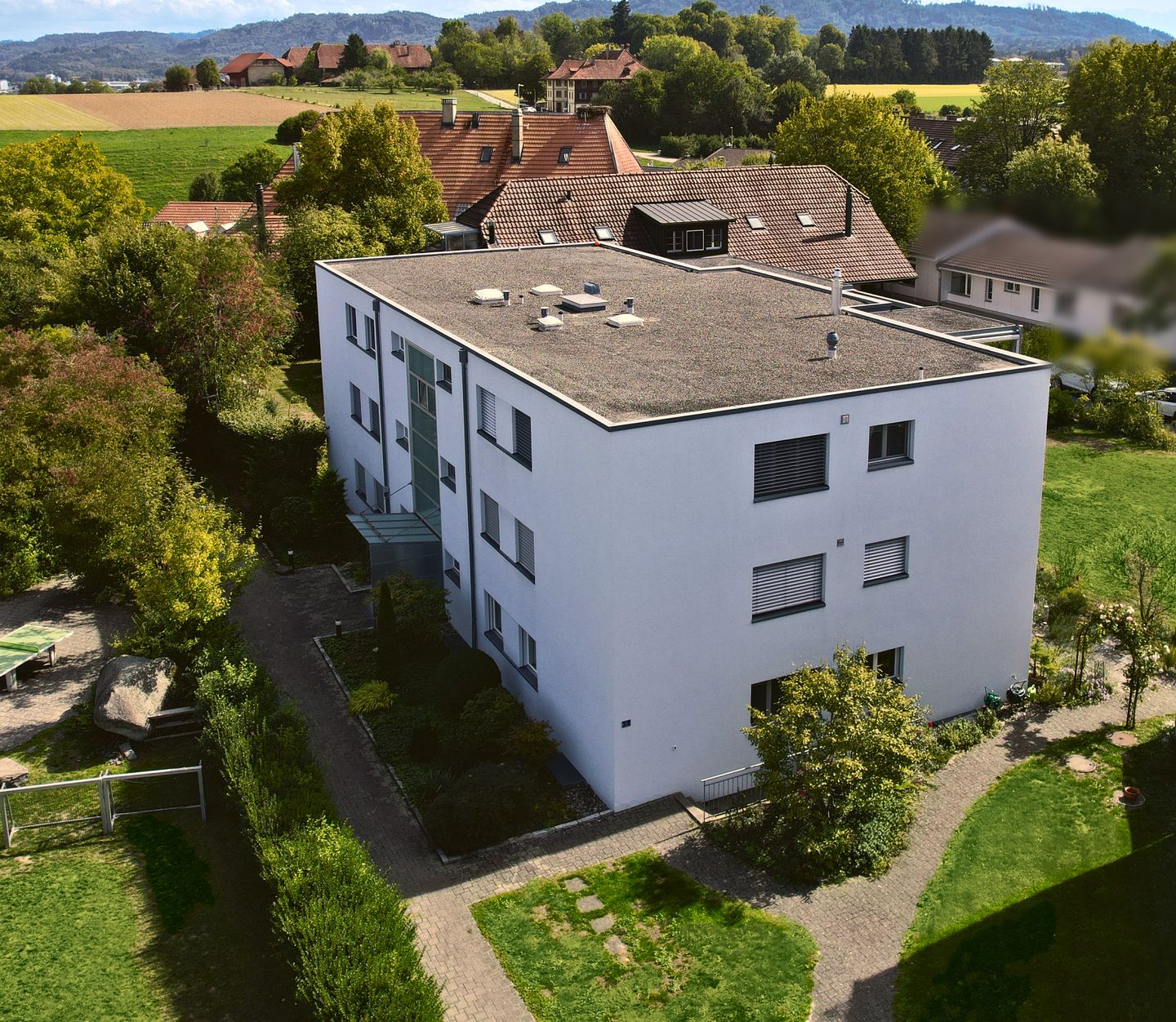 Luftaufnahme eines Mehrfamilienhauses mit Eigentumswohnungen und Garten in Münchenbuchsee